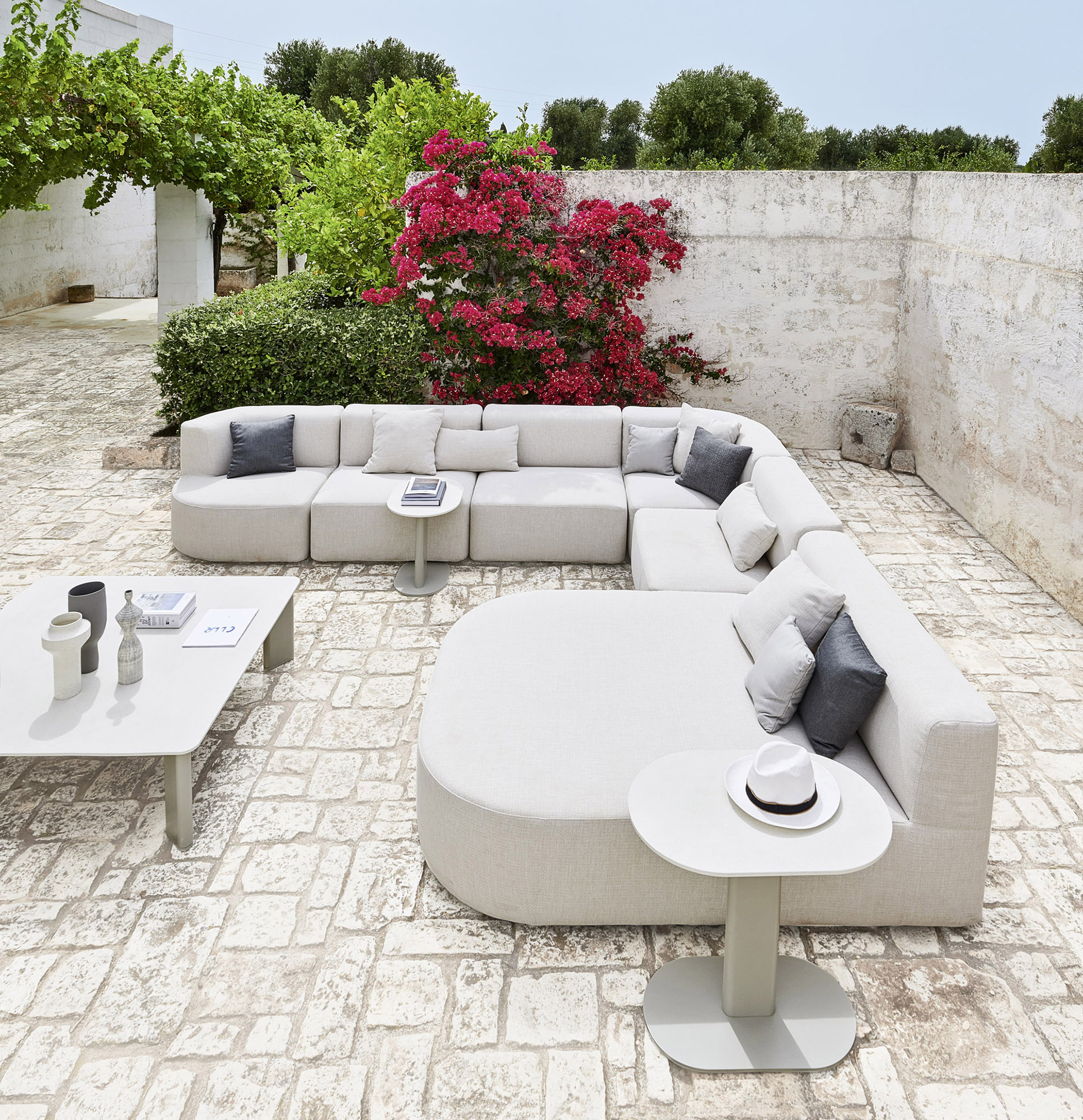 A whitewashed courtyard, modular seating in pale fabric, bougainvillea over the wall.