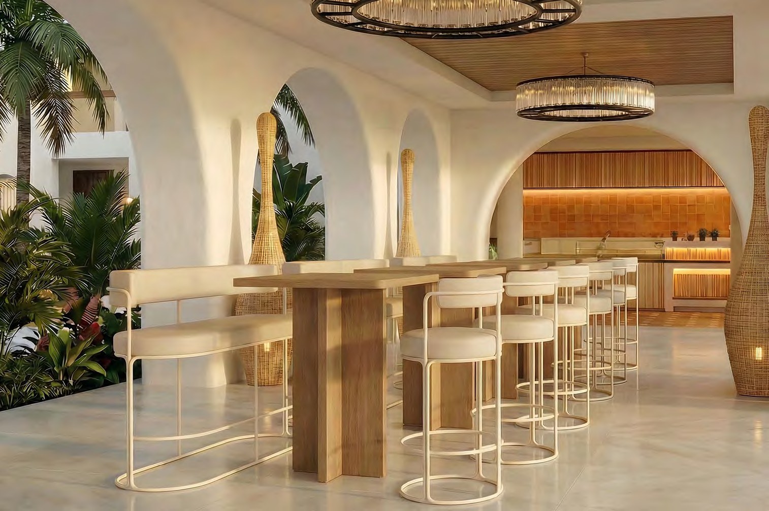Cream-framed high benches and bar stools with pale upholstered seats ranged along timber-topped bar-height tables in a white-plastered arched bar, palms and tropical planting visible through the arches at the left, tall woven rattan floor lanterns between them, two ringed chandeliers overhead and a lit timber and terracotta-tile back bar beyond.